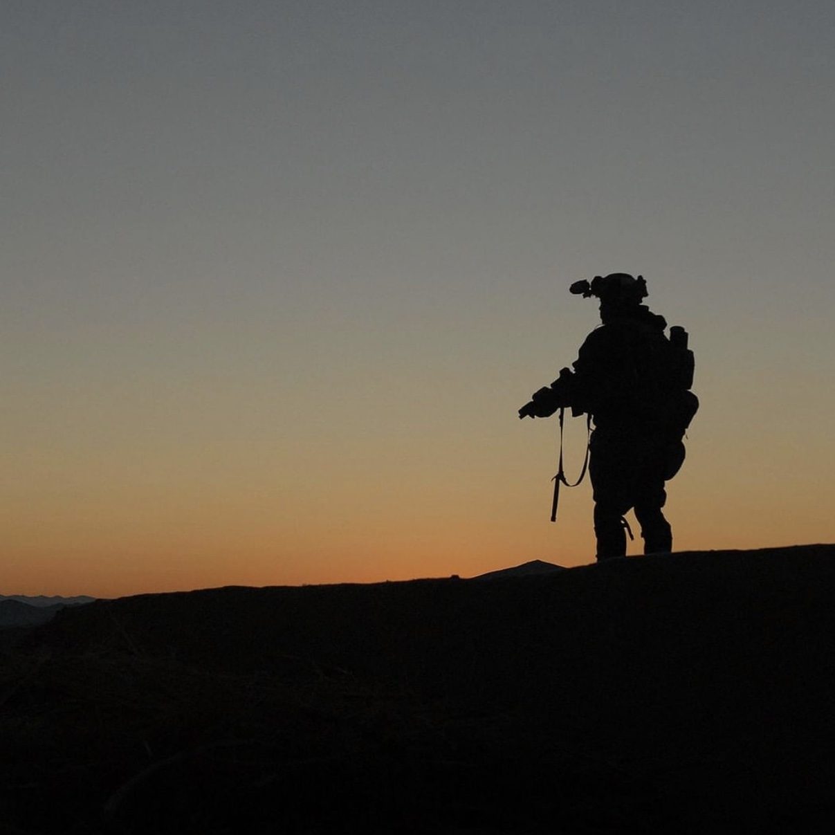 Silhouette of a soldier on a hill at sunset holding a firearm